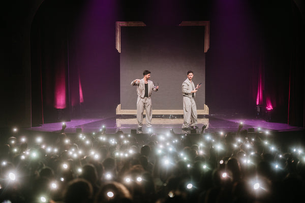 The French Twins on stage in front of a massive crowd holding phone lights.