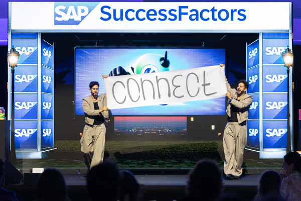The French Twins on a corporate convention stage with a branded LED backdrop.