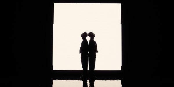 The French Twins as identical twin silhouettes facing each other on a brightly lit stage.