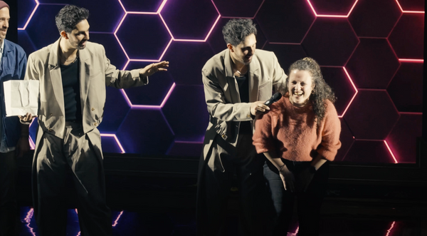 The French Twins on a televised magic stage interacting with a guest under hexagonal LED lighting.